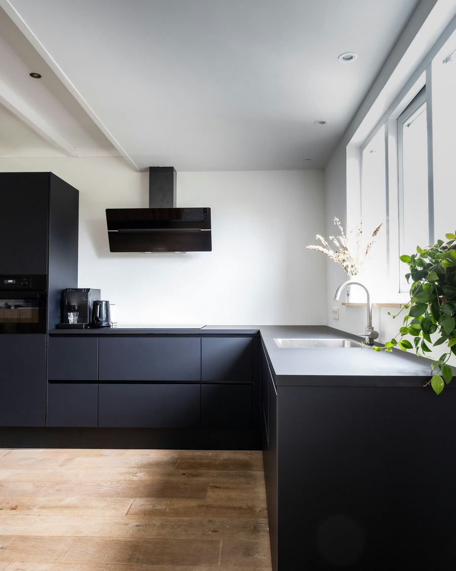 A kitchen with matte black cabinets and a white wall